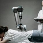 A woman receives a robotic massage as a scientist monitors, showcasing modern technology.
