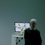 A senior adult sits indoors next to a computer wrapped in caution tape, symbolizing job loss and unemployment.