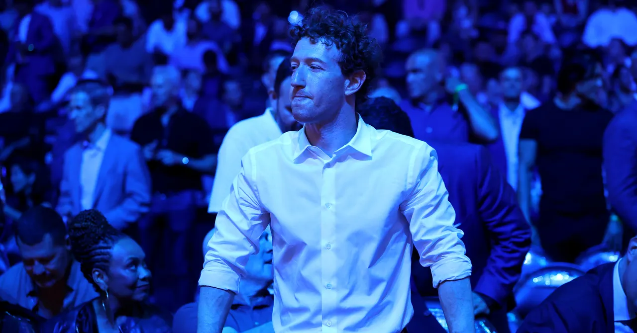 Man in white shirt stands in a crowded event, blue lighting casts over the audience.