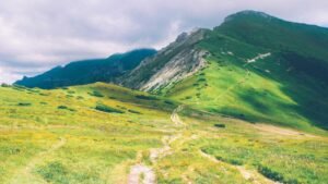 Lush green mountain landscape with a winding path under a cloudy sky