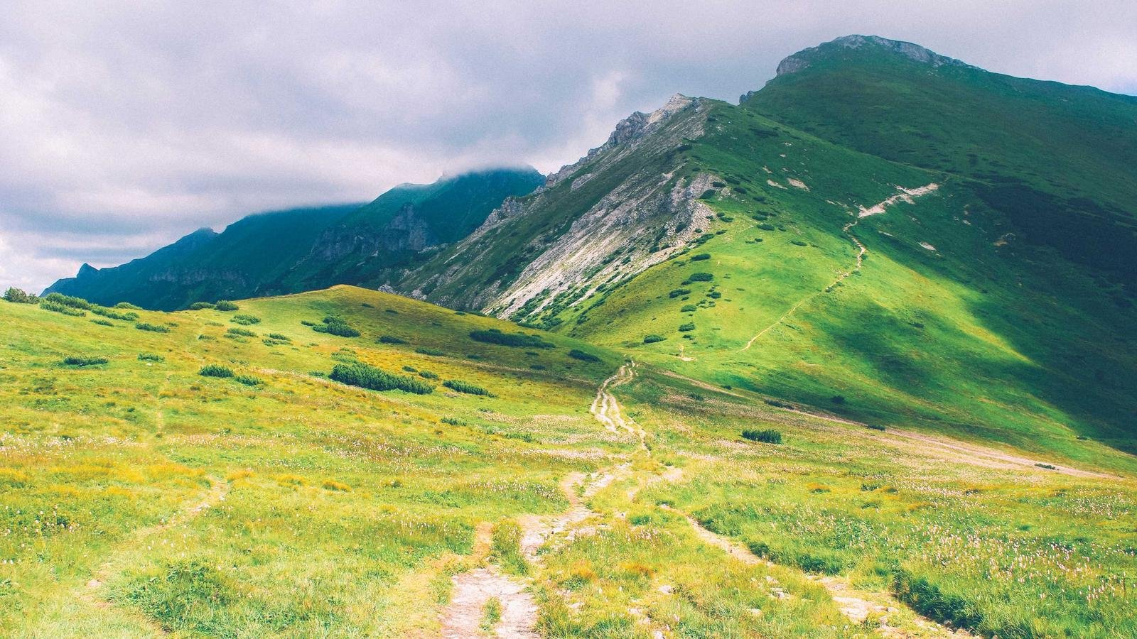Lush green mountain landscape with a winding path under a cloudy sky