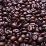 Close-up view of a large pile of roasted coffee beans, showing various shades of brown and glossy textures.