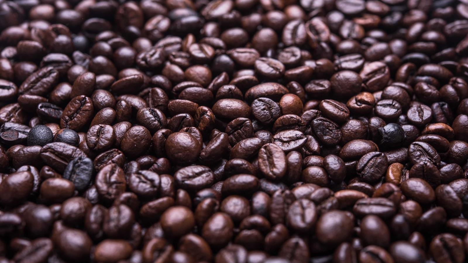 Close-up view of a large pile of roasted coffee beans, showing various shades of brown and glossy textures.