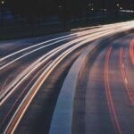 Long exposure of highway at night with red and white light trails showing vehicle motion, streetlights faintly visible.
