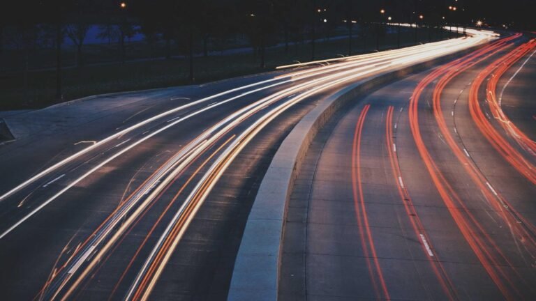 Long exposure of highway at night with red and white light trails showing vehicle motion, streetlights faintly visible.