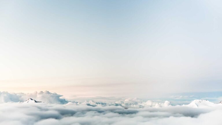 Snow-capped mountain peaks emerging through a blanket of clouds under a clear sky.