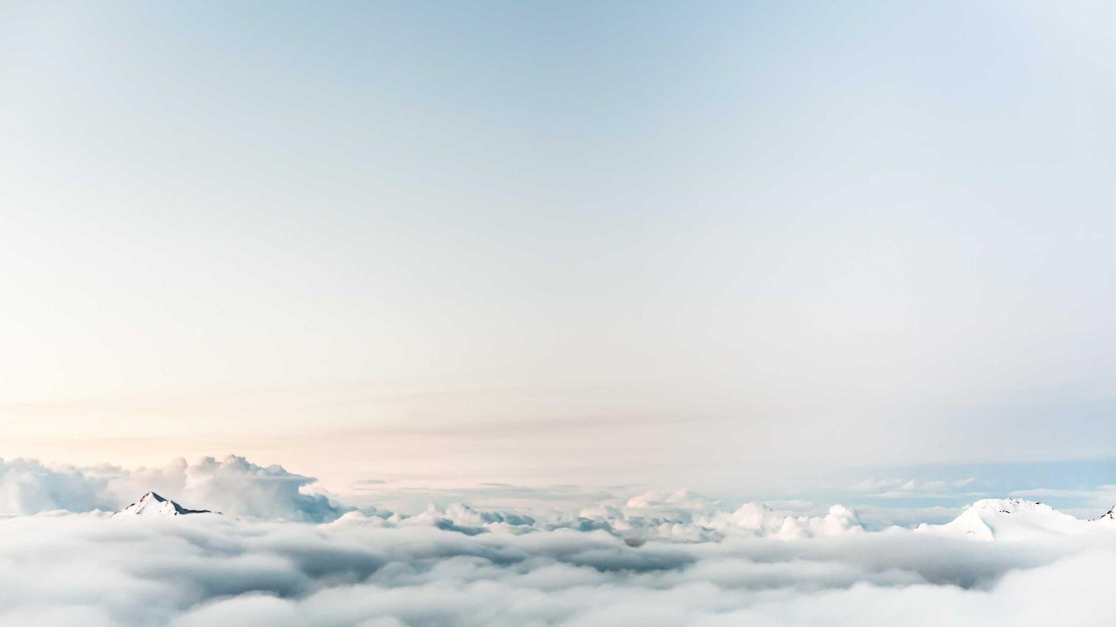 Snow-capped mountain peaks emerging through a blanket of clouds under a clear sky.