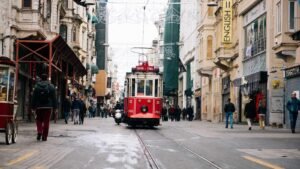 Red tram labeled "Taksim-Tünel" on a busy street with pedestrians and shops, including a sign for English courses.