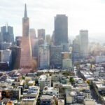 San Francisco skyline with iconic Transamerica Pyramid and surrounding skyscrapers under a bright, partly cloudy sky.