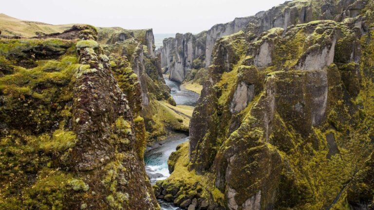 Lush green cliffs with a winding river flowing through a narrow canyon under a cloudy sky.