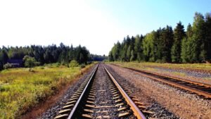 Railway tracks extending into the distance, flanked by green trees and grass under a clear blue sky.