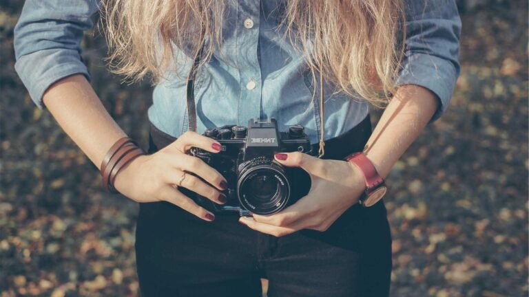 Person in a blue shirt holding a vintage camera outdoors, wearing a red watch and bracelet.