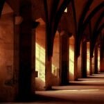 Arched hallway with warm sunlight casting shadows through windows onto the stone floor