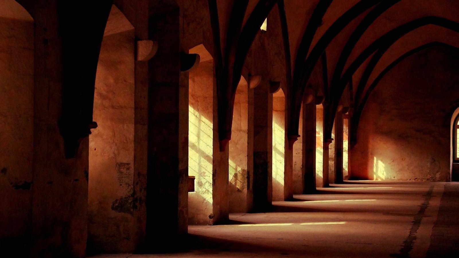 Arched hallway with warm sunlight casting shadows through windows onto the stone floor
