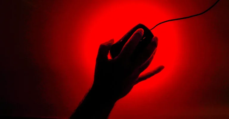 Silhouette of a hand holding a computer mouse against a bright red background.
