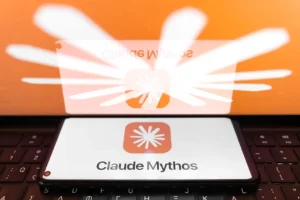 Smartphone displaying Claude Mythos app on screen, placed on a keyboard with an orange logo reflected in the background.