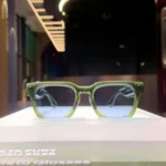 Green smart glasses displayed on a white platform, lit background with blurred room. On-screen text: Meta Fury SP/SU 2026,...