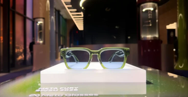 Green smart glasses displayed on a white platform, lit background with blurred room. On-screen text: Meta Fury SP/SU 2026,...