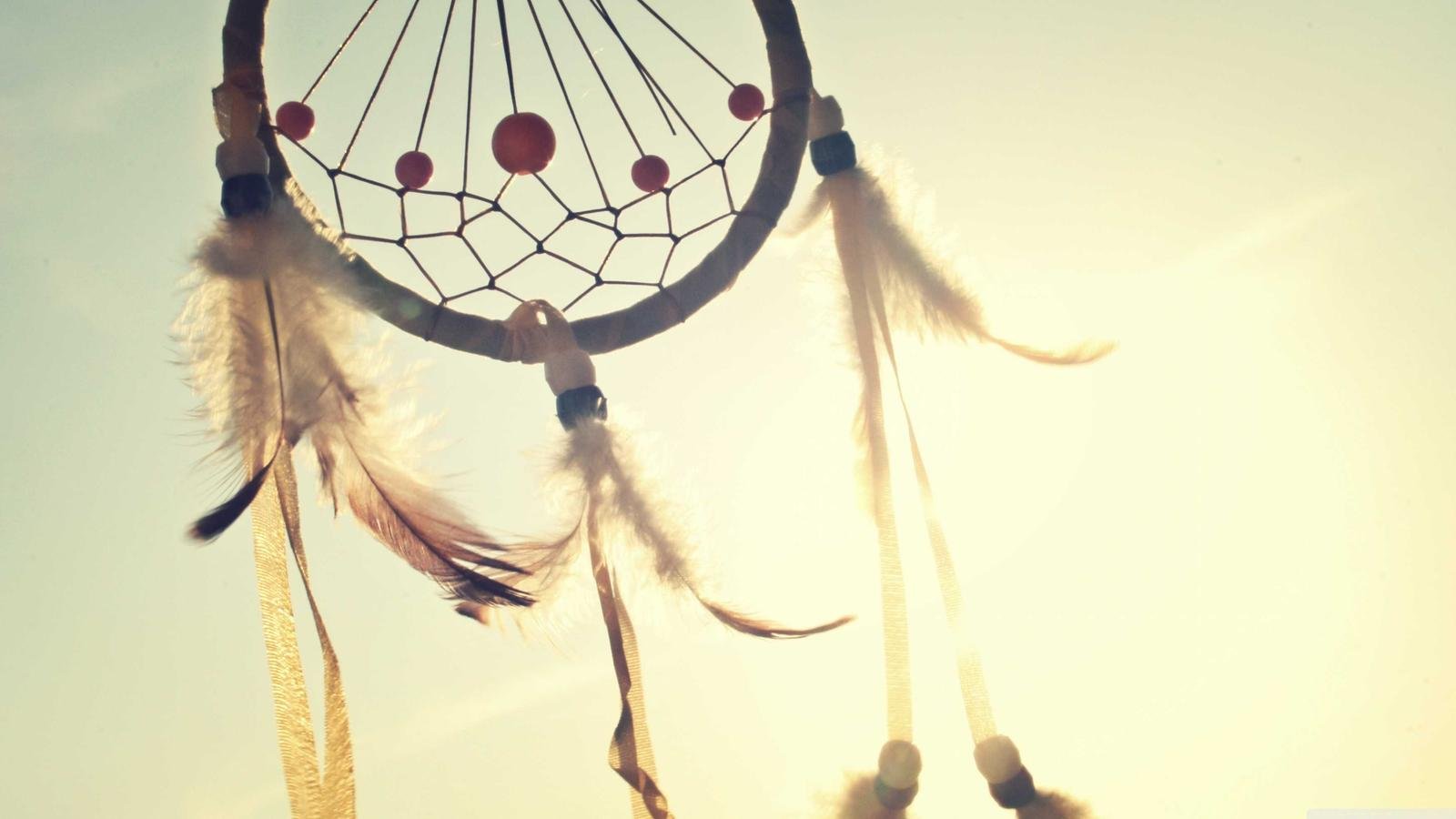 A dreamcatcher with feathers and beads hanging against a bright sky.