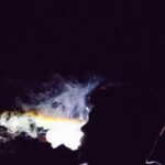 Silhouette of a person exhaling smoke against a dark background, with light illuminating the smoke trails.