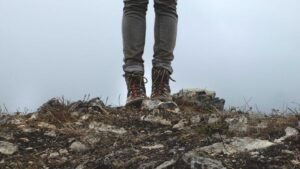 Person in hiking boots and jeans standing on rocky terrain with a foggy background.
