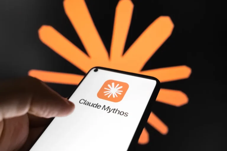 Smartphone displaying "Claude Mythos" logo and text, hand holding device, abstract orange design in background.