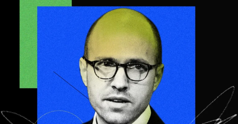 Man with glasses against a blue and green geometric background, wearing a suit and looking towards the camera.
