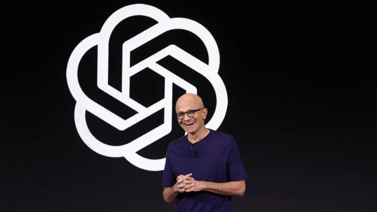 Smiling man in a dark shirt stands in front of a large, abstract logo on a black background.