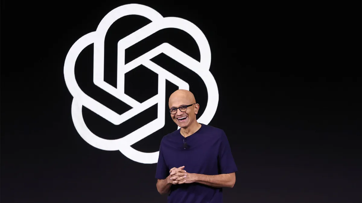 Smiling man in a dark shirt stands in front of a large, abstract logo on a black background.