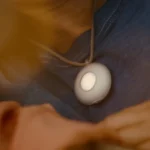 Person wearing a round, white pendant on a cord, resting on a blue shirt.