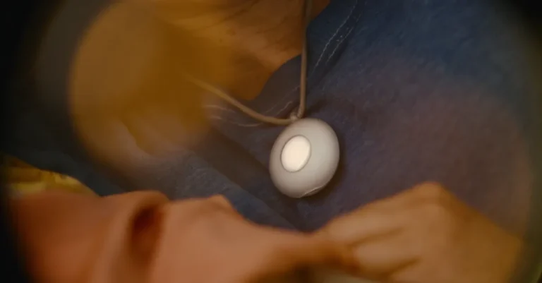 Person wearing a round, white pendant on a cord, resting on a blue shirt.
