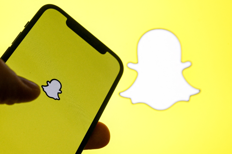 Smartphone displaying Snapchat logo on yellow screen, large Snapchat logo in the background, close-up view.