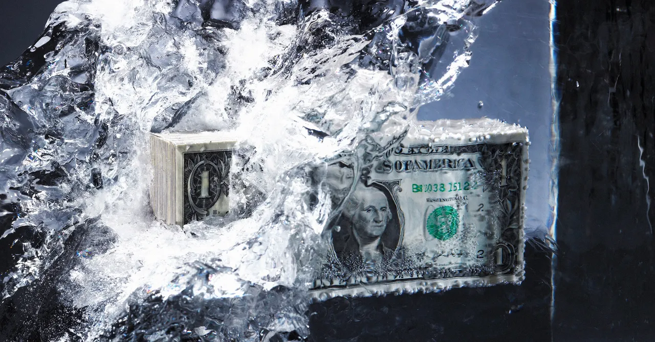 Stack of US dollar bills encased in ice, partially melting, with water splashing around.