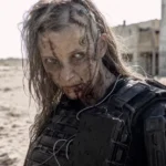 Zombie-like figure with scars and armored gear in a desolate, sandy landscape, abandoned building in the background.