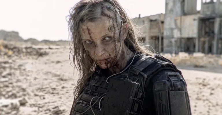 Zombie-like figure with scars and armored gear in a desolate, sandy landscape, abandoned building in the background.