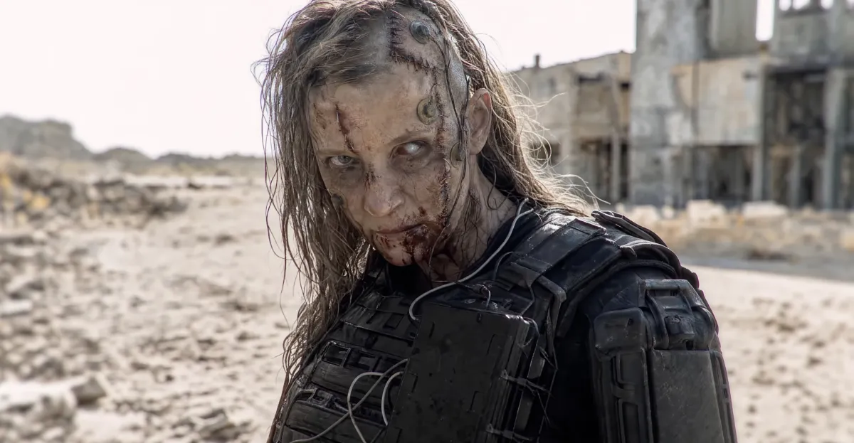 Zombie-like figure with scars and armored gear in a desolate, sandy landscape, abandoned building in the background.