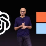 Person standing on stage with OpenAI and Microsoft logos in the background, wearing a dark shirt and glasses.