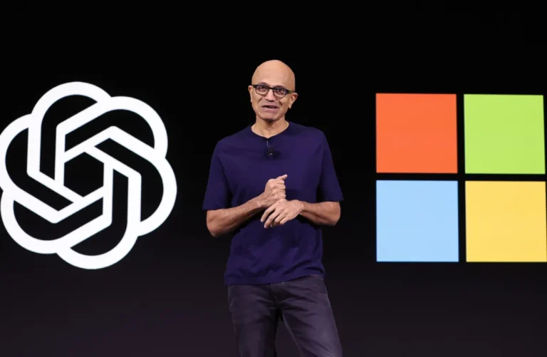 Person standing on stage with OpenAI and Microsoft logos in the background, wearing a dark shirt and glasses.