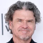 Man with gray hair and a slight smile against a backdrop with partial text "TR FEST".