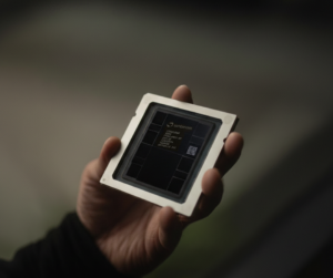 A hand holds a computer chip with visible text and QR code, blurred background.