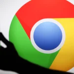 Silhouette of a hand holding a smartphone in front of a large Google Chrome logo.