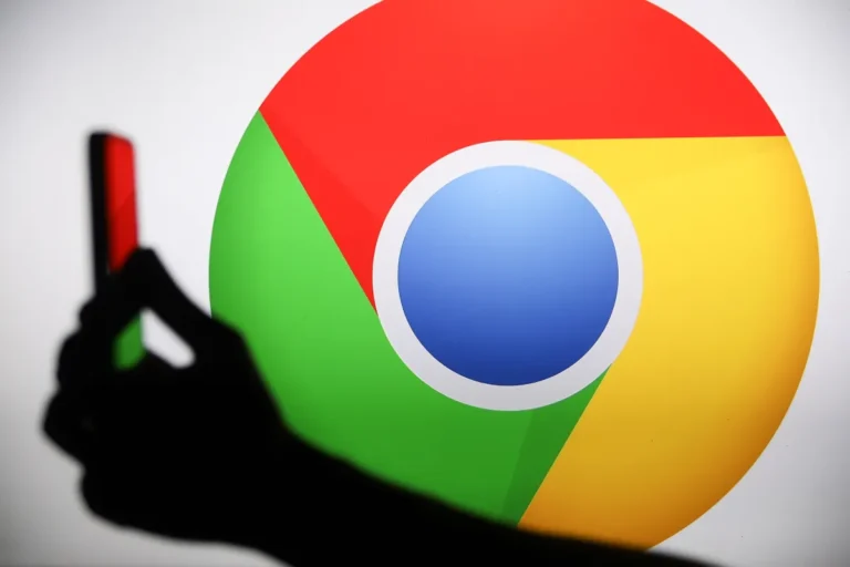 Silhouette of a hand holding a smartphone in front of a large Google Chrome logo.