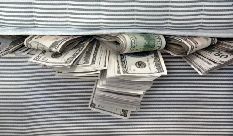Stacks and rolls of U.S. dollar bills hidden under a striped mattress.