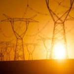 Silhouetted power lines and pylons at sunset with a bright orange sky.