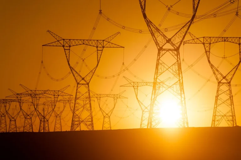 Silhouetted power lines and pylons at sunset with a bright orange sky.