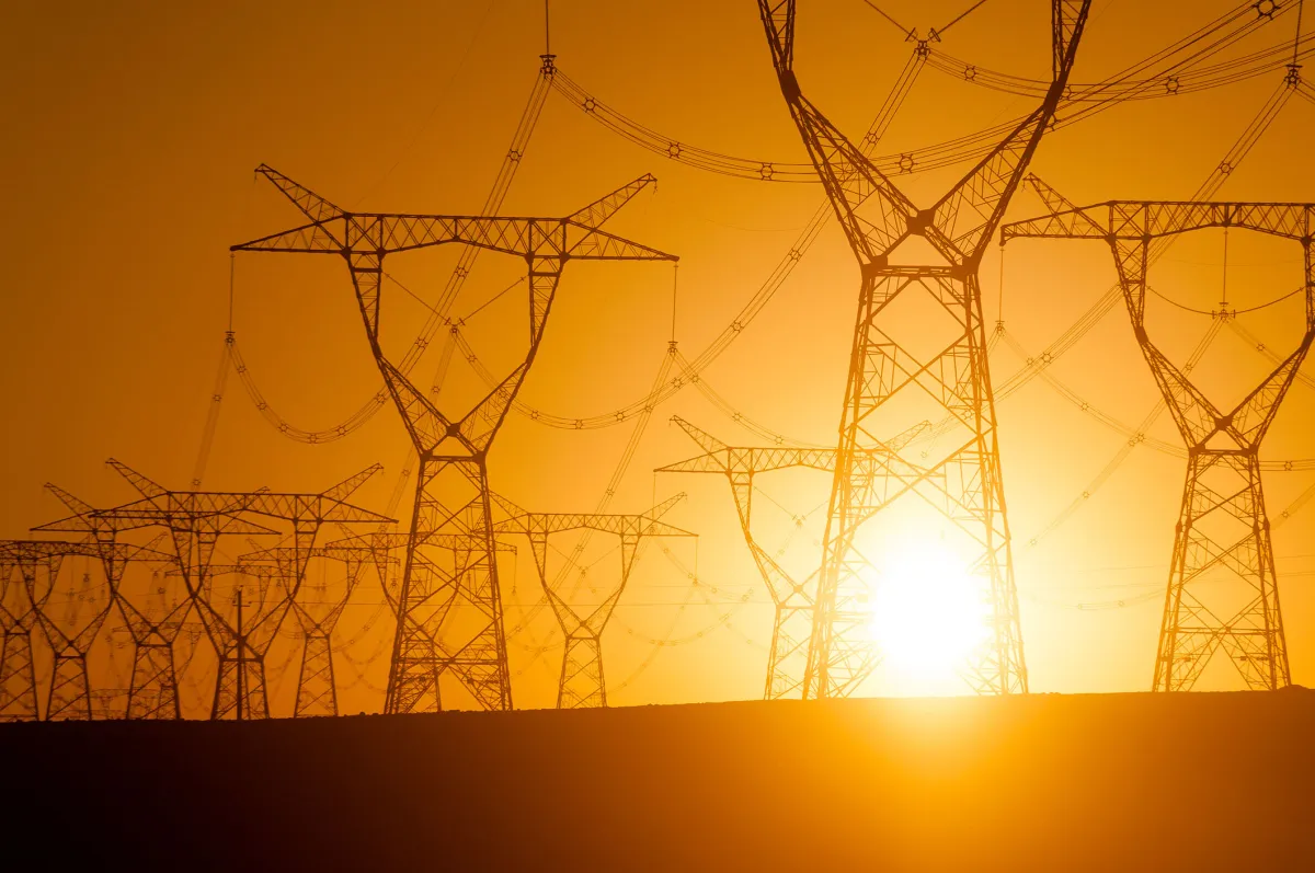 Silhouetted power lines and pylons at sunset with a bright orange sky.