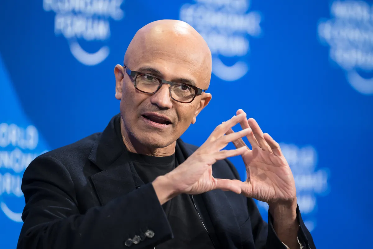 Bald man in glasses speaking, hands gesturing, blue background with blurred text "World Economic Forum".