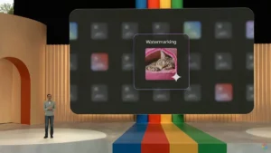 Person on stage with a large screen displaying a cat image labeled "Watermarking," colorful stripes on the floor.