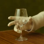 Robot hand with five fingers holding a wine glass on a wooden table, against a blurred green background.
