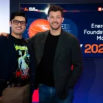 Two people smiling in front of a screen displaying "Energy's Foundation Model" and "2026" with logos for Applied Computing...